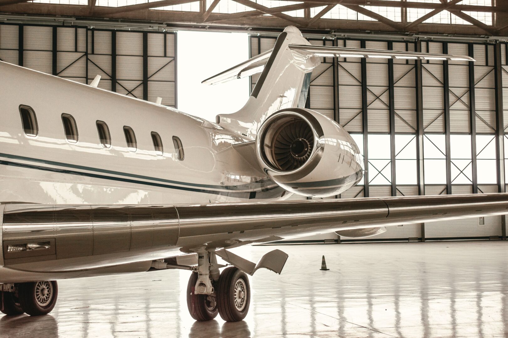 A business jet parked in a hangar, seen beside the wing, with its rear engine and tail in view