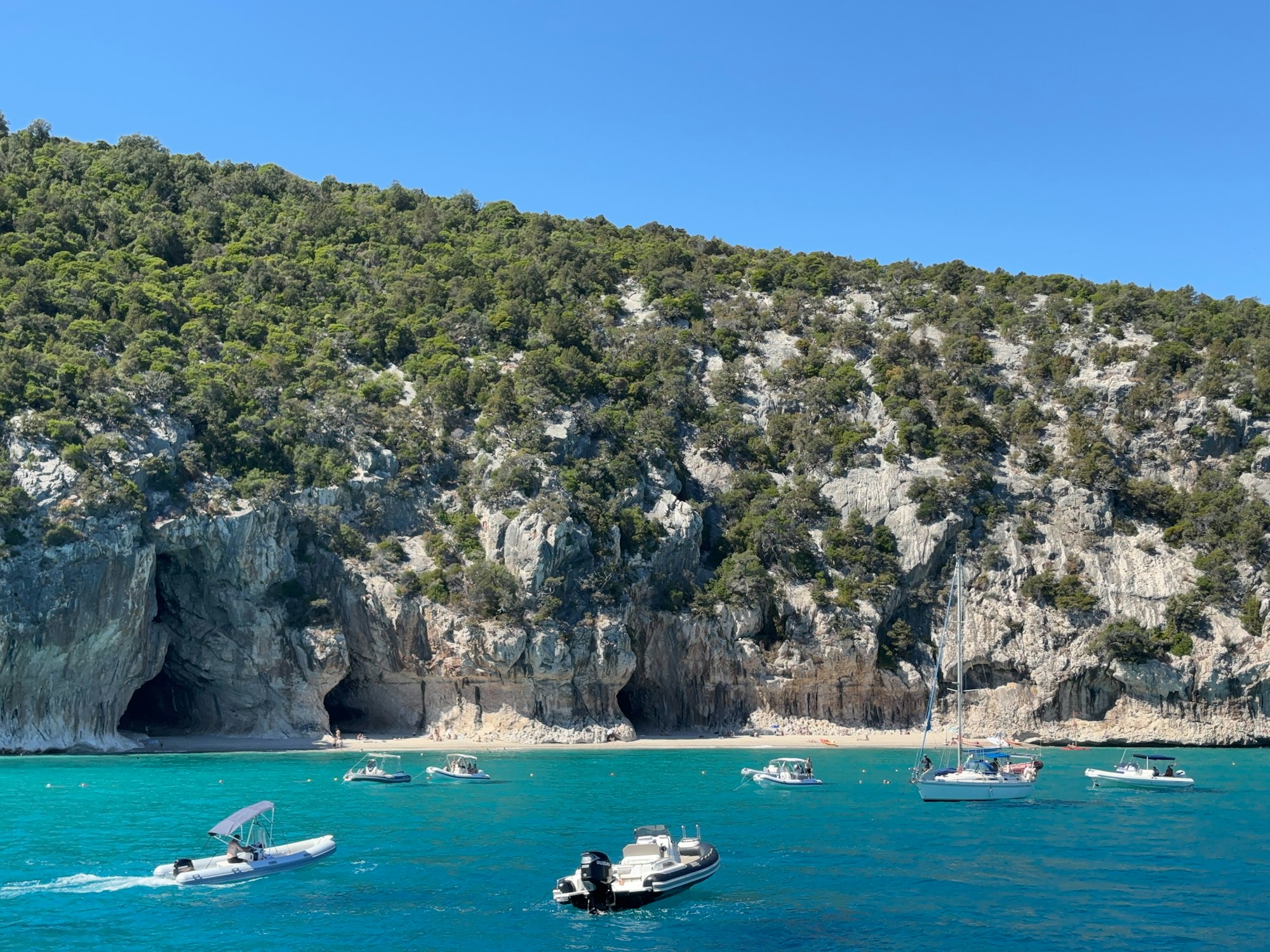Boats at anchor in turquoise water below rocky cliffs